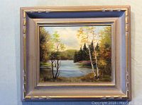 Overall view of the framed oil painting of a lake and trees, showing the entire artwork and frame.