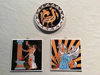 Lot showing two square hand painted tiles and one round decorative plate arranged on light fabric background.