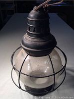 Full view of black metal railway lantern with globe and wire cage on table.