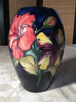 Front and side view of oval ceramic vase with raised pink, yellow flowers and green leaves on deep blue background.