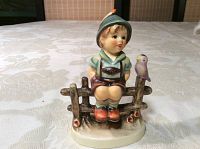 Front left angled view of the Goebel porcelain figurine of a boy sitting on a fence with a bird