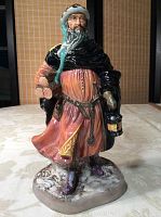 Front view of Good King Wenceslas figurine showing detailed painted face, holding lantern in right hand and roses in left, standing on snowy base.