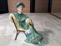 Front view of the seated lady figurine in green dress and hat, showing detailed paintwork and chair.