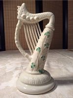 Front diagonal view of the porcelain Irish harp figurine showing the textured body, green shamrocks, and round base.