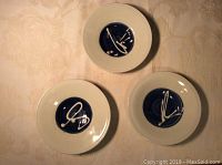 Top view of three small white wall hanging dishes with deep blue centers and abstract white brushstroke decoration.