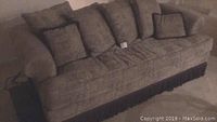 Front and angled view of taupe sofa with loose cushions and dark fringe trim on bottom