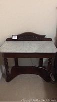Full view of the mahogany wood entry table with white marble slab top showing the turned legs and carved back panel.