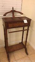 Full front view of the wooden valet stand showing the clothing hanger top, drawer, and legs.