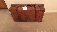 Front view of old worn brown leather suitcase with visible wear and leather straps for closure.