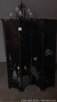 Black lacquer side of the screen with crane and floral designs visible in dim light
