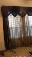 Full view of double window treatment with bronze sheers covering window and layered dark fabric draped top