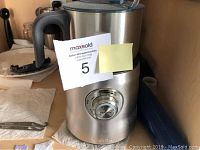 Silver Breville milk frother and heater with black handle, viewed from front showing rotary dial and MaxSold lot tag attached.