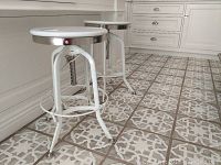 Two white metal counter stools with round seats and adjustable height levers, placed on patterned tile floor in kitchen area.