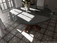 Round kitchen table with glass top showing light reflection and flower vase in sunlight