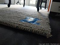 Close-up of rug edge showing chunky looped weave and blue tape with measurement note
