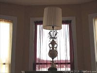 Full height view of the ornate 42-inch table lamp showing sculpted base and white pleated shade in front of window.
