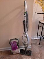 Full view of the Shark Professional Multi-Steam Pocket steam cleaner standing against wall with bag of attachments.