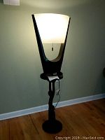 Photo of tall floor stand with illuminated cream shade and dark sculptural base, shows design and height