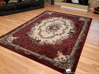 Area rug with central floral medallion and burgundy border on hardwood floor.