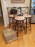 Five bar stools with metal frames and light beige upholstered round seats. Four stools are assembled and one is in its original cardboard box. One seat has visible rip damage.