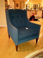 Front-left angled view of blue upholstered accent chair showing nail head trim and wooden legs.
