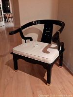 Front view of black wooden chair with beige cushion showing curved backrest and gold accent details.