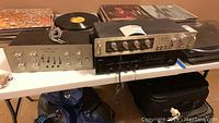 Three audio components on folding table with vinyl records nearby