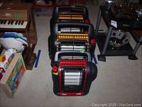 Three portable propane heaters lined up on floor, front view.