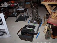 Keystone dual projector, Sony video recorder, vintage electric iron, and metal canister with nozzle in storage area on floor.