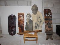 Two wooden carved wall hangings and a wicker stool with carved wooden item on top, plus painted cutout artwork of two figures.