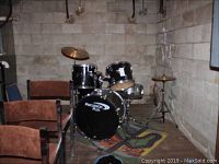 Full view of black drum kit setup in basement corner with chairs