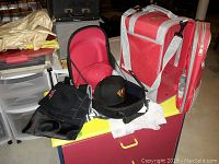 Photo of red and black New Era Cap Carrier, two baseball caps (black and red), and red/gray gym bag on table