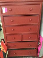 Front view of the red wood dresser showing all seven drawers and wooden knobs.