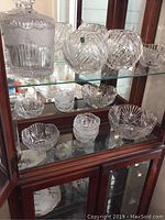 Display cabinet shelf with assorted Marc Aurel crystal pieces including bowls and candle holders.