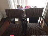 Photo showing two dark brown wicker bar stools with black metal frames placed in front of a black desk with office supplies on it.