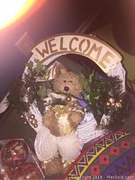 Welcome wreath with a teddy bear, greenery, golden glittery bow and assorted small ornaments