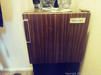Full view of dorm fridge showing wood grain exterior, silver handle, and Excellence brand sticker on door.