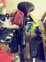 Photo of the elliptical machine showing the padded black seat, mechanical base, and some clutter around it.
