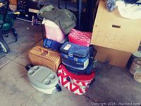Photo showing a stack of 2 wicker picnic baskets, 7 various coolers including a red-and-white patterned cooler and a cooler with control panel, along with some other bags and chairs.