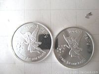 Photo showing the front side of two silver Tooth Fairy coins depicting a fairy holding a star wand and text referencing trade for a tooth.
