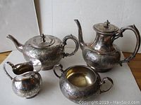 Front view of four-piece silver plated tea and coffee set showing teapot, coffee pot, creamer, and sugar bowl with detailed scrollwork engravings.