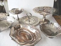 Six vintage silver plated pierced and reticulated serving plates and trays arranged on white background showcasing varied shapes and intricate cut-out patterns.