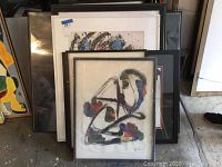 Photo of five original framed abstract art pieces stacked together, showing varied frame colors and signatures.