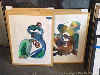 Front view of two framed abstract watercolors with gold frames and white mats