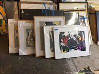 Group view of five framed abstract artworks leaning against wall
