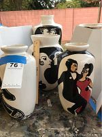 Four white glazed ceramic vases with black and red figurative designs and a ruler for scale.