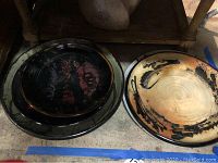 Stacked small black platter with red decoration atop larger plain black platter and one tan/orange platter