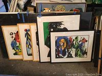 Grouping of five framed artworks by Jenik Cook, showing two gold-framed watercolors, one black-framed splash, one black-framed silhouette, and one additional framed piece