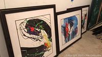 Three framed abstract paintings leaning against wall