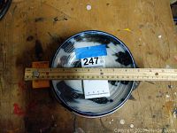 Top view of black and white glazed saucer with ruler measuring approx. 7-inch diameter.